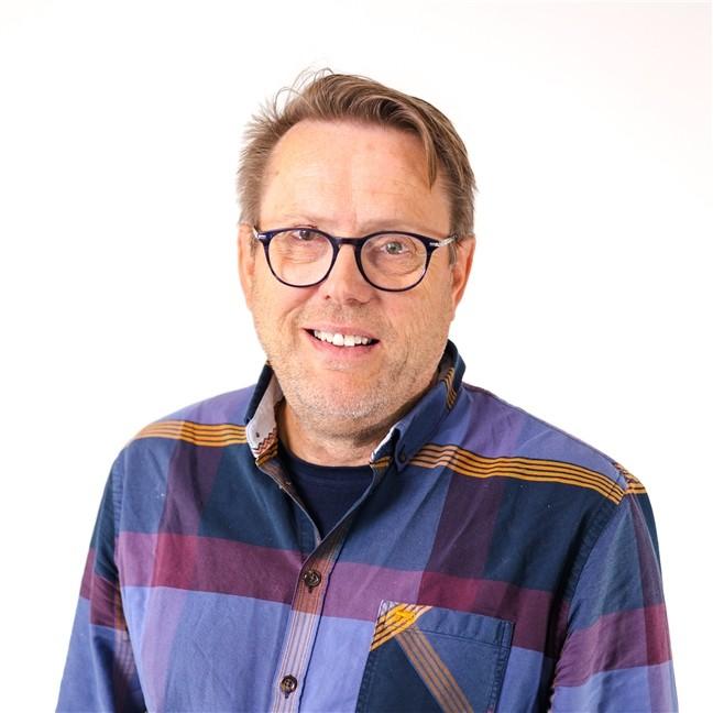 Mann med lyst hår og briller iført en blå- og lillarutete skjorte. Hvit bakgrunn.