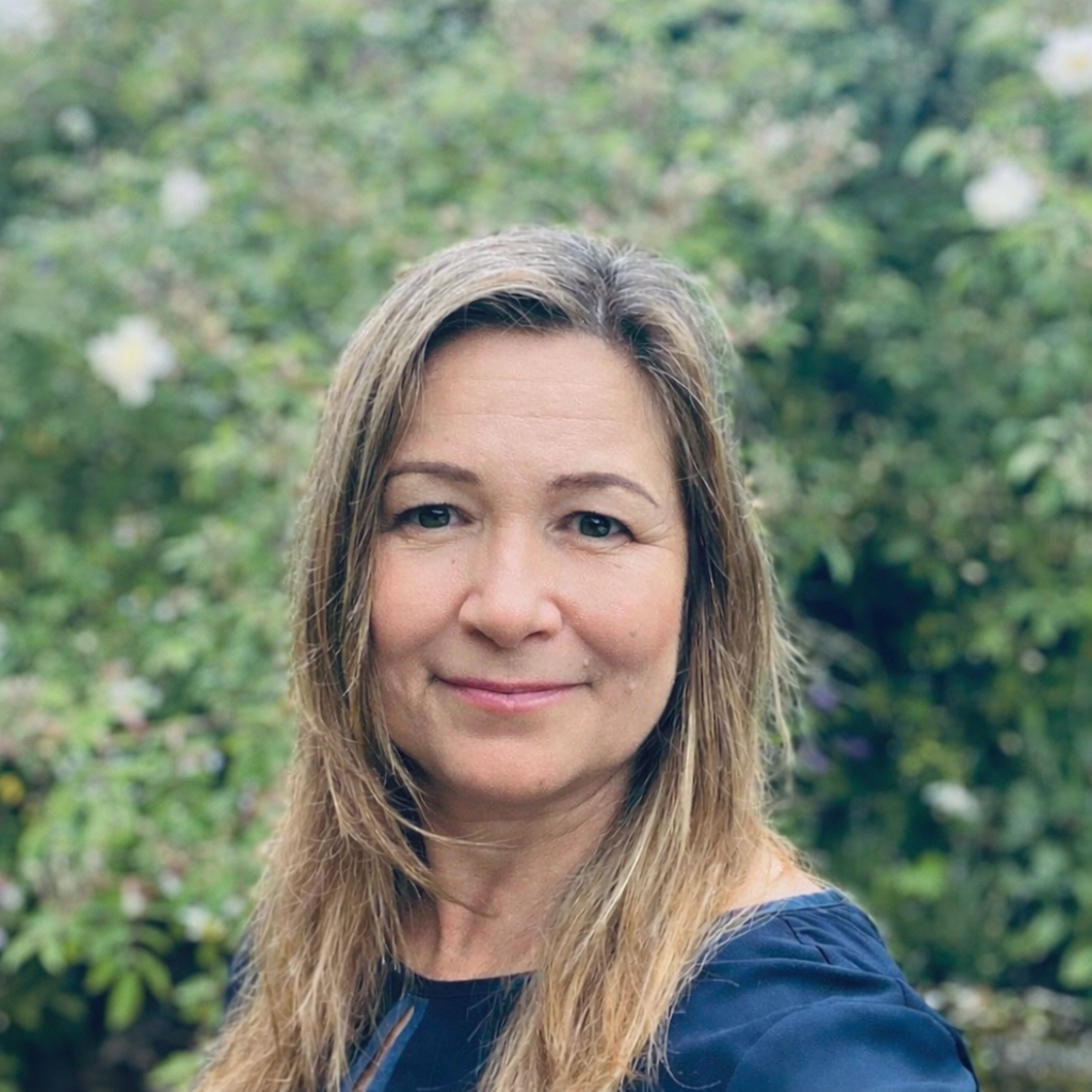 Portrettbilde av voksen kvinne. Hun står ute foran noen grønne busker og trær. Sonja Cassidy.